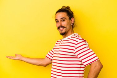 Sarı arka planda uzun saçlı beyaz bir genç hoş bir yüz ifadesi sergiliyor..