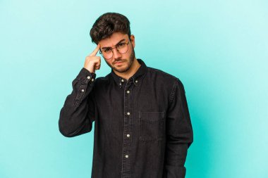 Mavi arka planda izole edilmiş genç beyaz bir adam şakağı parmağıyla işaret ediyor, düşünüyor ve bir göreve odaklanıyor..