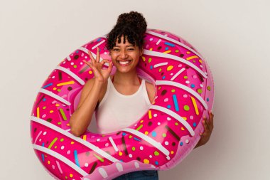 Genç melez kadın elinde şişme bir donut tutuyor beyaz arka planda izole edilmiş neşeli ve kendinden emin bir şekilde iyi niyet gösteriyor..