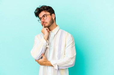 Kafkasyalı genç bir adam mavi arka planda izole edilmiş. Bir strateji planlıyor, bir iş yolu düşünüyor..