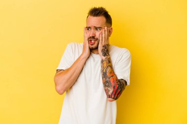 Genç dövmeli beyaz adam sarı arka planda izole edilmiş korkmuş ve korkmuş..