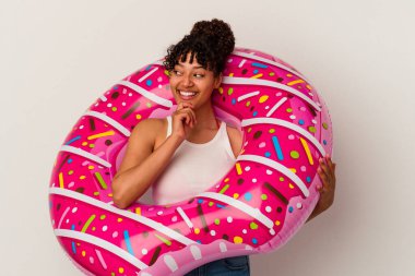 Beyaz arka planda izole edilmiş şişme bir donut tutan genç melez kadın şüpheli ve şüpheci bir ifadeyle yan yana bakıyor..