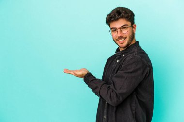 Mavi arka planda izole edilmiş genç beyaz bir adam palmiyesinde bir kopya alanı tutuyor..