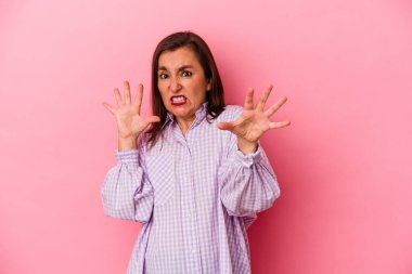 Pembe arka planda izole edilmiş orta yaşlı beyaz kadın pençelerini kedi taklidi yaparken gösteriyor, agresif bir hareket..