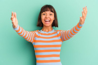 Genç melez kadın mavi üzerine izole edilmiş zaferi ya da başarıyı kutluyor, şaşırıyor ve şok oluyor..