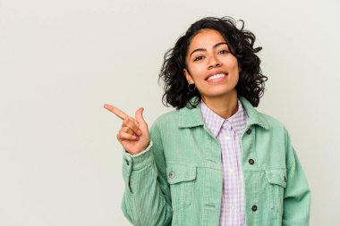 Beyaz arka planda izole edilmiş genç kıvırcık Latin kadın gülümsüyor ve boş alanda bir şeyler gösteriyor..