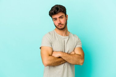 Kafkasyalı genç adam mavi arka planda izole edilmiş şüpheli, belirsiz, seni muayene ediyor..