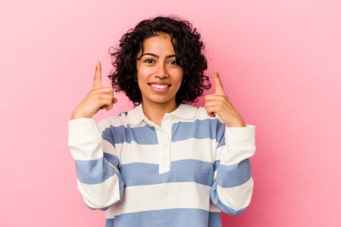 Pembe arka planda izole edilmiş genç kıvırcık Latin kadın işaret ediyor..