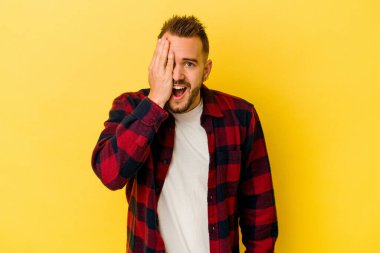 Sarı arka planda izole edilmiş genç dövmeli beyaz adam yüzünün yarısını palmiye ile kaplayarak eğleniyor..