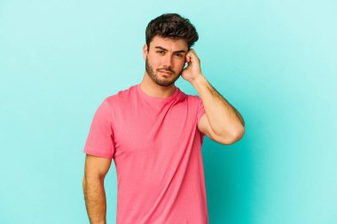 Genç beyaz adam mavi arka planda izole edilmiş parmaklarıyla kulaklarını kapatıyor, gürültülü bir ortam tarafından stresli ve umutsuz..