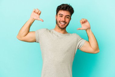 Mavi arka planda izole edilmiş genç beyaz adam gururlu ve kendinden emin hissediyor, örnek olarak.