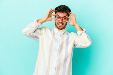 Mavi arka planda izole edilmiş genç beyaz adam bir başarı fırsatı bulmak için gözlerini açık tutuyor..