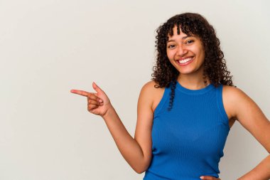 Beyaz arka planda izole edilmiş genç melez kadın işaret parmağıyla işaret ederek neşeyle gülümsüyor..