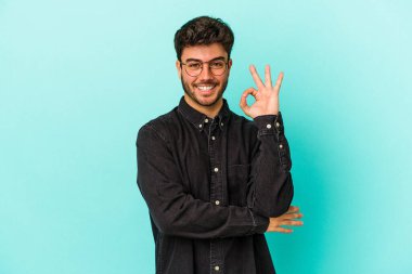 Kafkasyalı genç bir adam mavi arka planda izole edilmiş bir şekilde göz açıp kapayana kadar iyi bir el hareketi yapıyor..