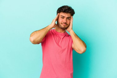 Genç beyaz adam mavi arka planda izole edilmiş tapınaklara dokunuyor ve başı ağrıyor..
