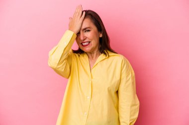 Orta yaşlı beyaz bir kadın pembe arka planda izole edilmiş bir şekilde bir şeyi unutuyor. Alnına avuç içi ve kapalı gözlerle vuruyor..