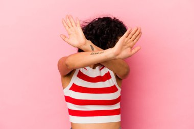 Genç kıvırcık Latin kadın pembe arka planda izole edilmiş iki kolu çapraz tutuyor, inkar kavramı.