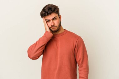 Beyaz arka planda izole edilmiş genç beyaz bir adam yorgun ve uykulu bir şekilde elini başının üstünde tutuyor..