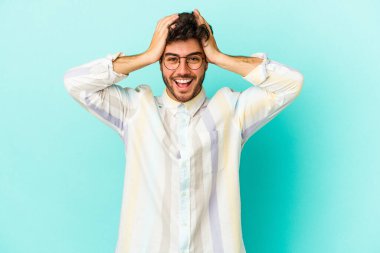 Genç beyaz adam mavi arka planda izole edilmiş bağırıyor, çok heyecanlı, tutkulu, bir şeyden memnun..