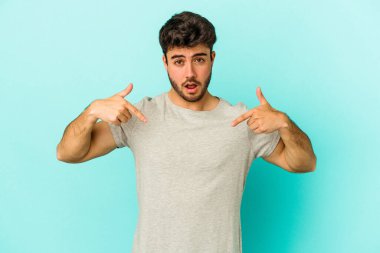 Kafkasyalı genç adam mavi arka planda izole edildi. Parmakları aşağıda, olumlu bir his var..