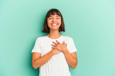 Genç melez kadın mavi renkte izole edilmiş gülüyor ellerini yüreğinde tutuyor, mutluluk kavramını koruyor..