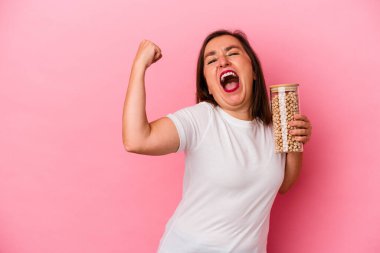 Orta yaşlı, elinde nohut kavanozu olan beyaz bir adam pembe arka planda izole edilmiş bir şekilde zafer kazandıktan sonra yumruğunu kaldırıyor..