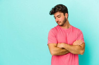 Mavi arka planda izole edilmiş genç beyaz adam kollarını kavuşturarak gülümsüyor..