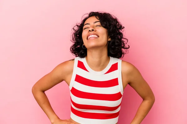 Young curly latin woman isolated on pink background relaxed and happy laughing, neck stretched showing teeth.