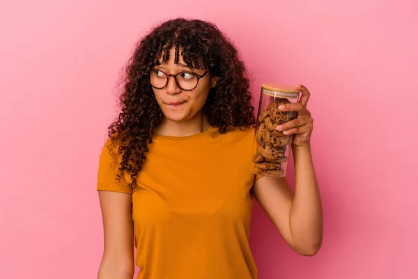 Jovem Mista Segurando Frasco Biscoitos Isolado Fundo Rosa Confuso Sente — Fotografia de Stock