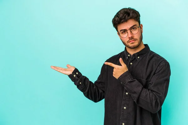 Jovem Caucasiano Isolado Fundo Azul Animado Segurando Espaço Cópia Palma — Fotografia de Stock