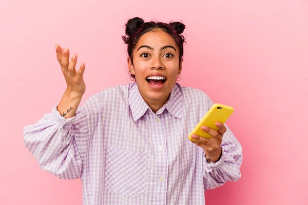 若いですラテン女性を保持しています携帯電話隔離ピンクの背景に楽しい驚きを受けます 興奮し 手を上げます — ストック写真