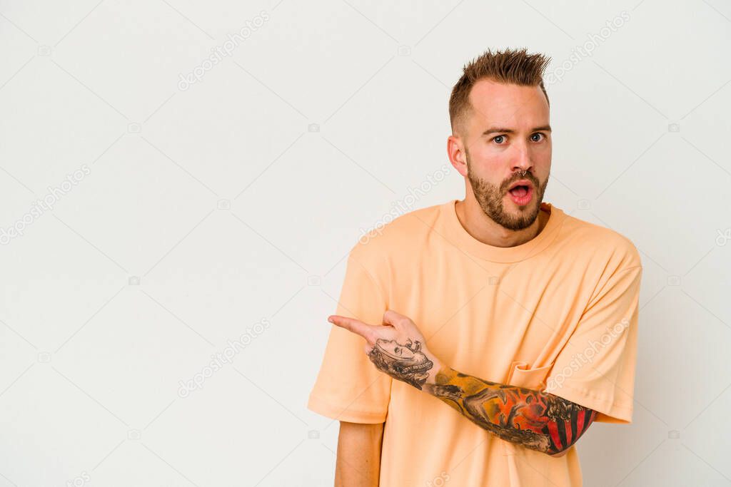 Young tattooed caucasian man isolated on white background smiling and pointing aside, showing something at blank space.