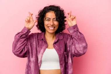 Pembe arka planda izole edilmiş genç kıvırcık Latin kadın şans getirsin diye dua ediyor.