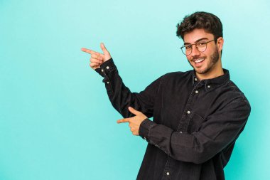 Kafkasyalı genç adam mavi arka planda izole edilmiş. İşaret parmağıyla işaret ettiği için heyecanlı..