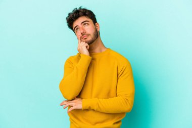 Kafkasyalı genç bir adam mavi arka planda izole edilmiş. Bir strateji planlıyor, bir iş yolu düşünüyor..