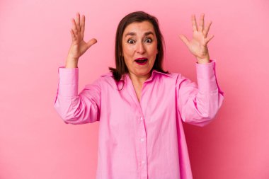 Pembe arka planda izole edilmiş orta yaşlı beyaz kadın zaferi ya da başarıyı kutluyor, şaşırıyor ve şok oluyor..