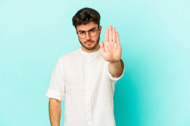 Mavi arka planda izole edilmiş genç beyaz adam elini uzatmış, dur işareti göstererek seni engelliyor..