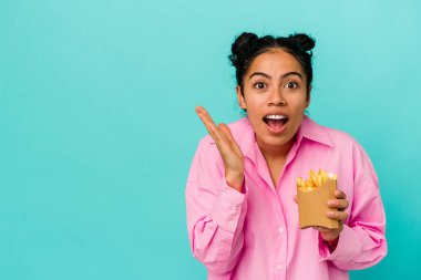 Mavi arka planda çipleri tutan genç Latin kadın şaşırdı ve şok oldu..