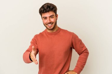 Beyaz arka planda izole edilmiş genç beyaz bir adam selamlama jesti olarak kameraya elini uzatıyor..