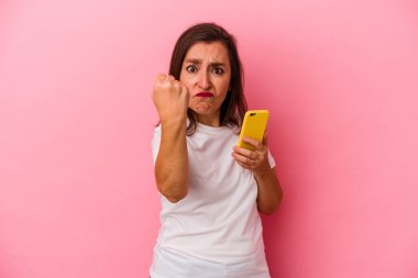 Elinde cep telefonu olan orta yaşlı beyaz bir kadın pembe arka planda izole edilmiş. Kameraya yumruk, agresif yüz ifadesi gösteriyor..