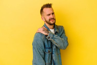 Sarı arka planda izole edilmiş, omuz ağrısı olan genç, dövmeli beyaz bir adam..