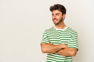 Beyaz arka planda izole edilmiş genç beyaz adam kollarını kavuşturarak gülümsüyor..