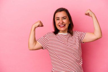 Orta yaşlı beyaz kadın pembe arka planda izole edilmiş zafer kazandıktan sonra yumruğunu kaldırıyor, kazanan konsept..