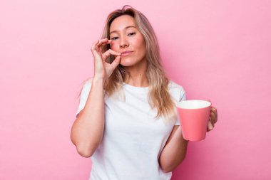 Genç Avustralyalı bir kadın pembe bir kupa tutuyor. Pembe arka planda izole edilmiş. Parmakları dudaklarında..