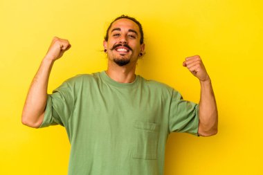 Sarı arka planda izole edilmiş uzun saçlı beyaz bir genç özel bir günü kutluyor, atlıyor ve enerji dolu kollarını kaldırıyor..