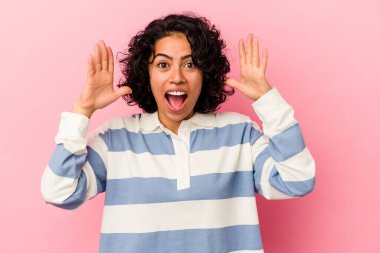 Pembe arka planda izole edilmiş genç kıvırcık Latin kadın zaferi veya başarıyı kutluyor, şaşırıyor ve şok oluyor..