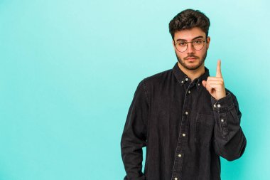 Mavi arka planda izole edilmiş genç beyaz adam bir numarayı parmağıyla gösteriyor..