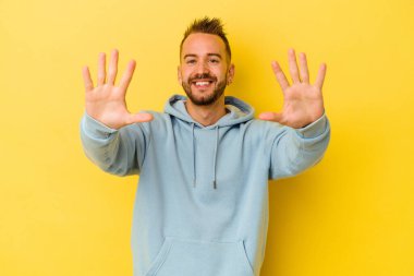 Sarı arka planda izole edilmiş genç dövmeli beyaz adam on numarayı elleriyle gösteriyor..