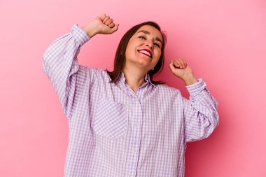 Pembe arka planda soyutlanmış orta yaşlı beyaz bir kadın özel bir günü kutluyor, atlıyor ve enerjiyle kollarını kaldırıyor..