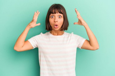 Genç melez kadın mavi üzerine izole edilmiş zaferi ya da başarıyı kutluyor, şaşırıyor ve şok oluyor..